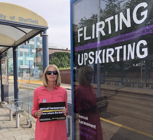 Know The Line member standing next to a sign saying 'Flirting Upskirting' on a Sheffield tram stop